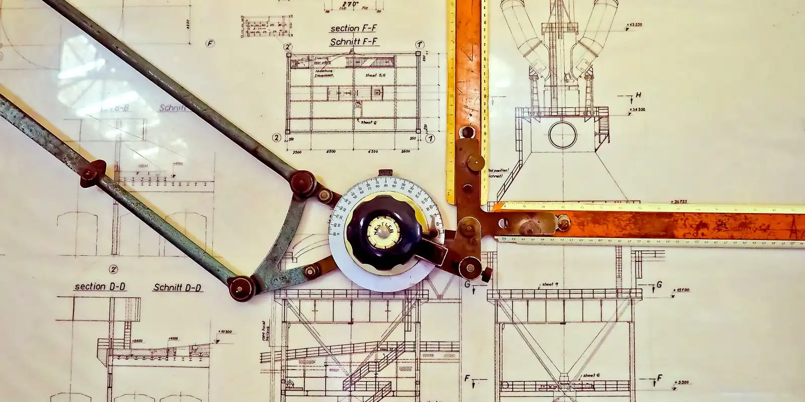 Technical drawings pinned under a drafting arm with a round protractor head