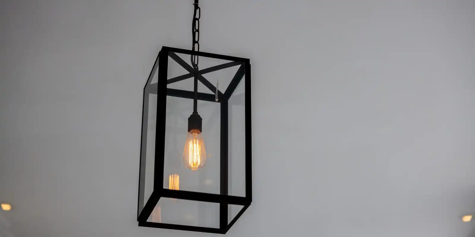 A glass and black metal pendant with a glowing filament bulb against a pale grey ceiling