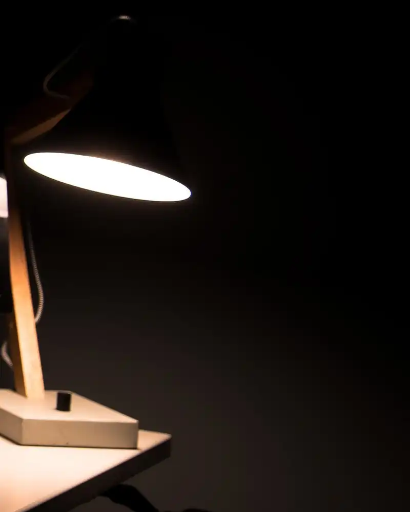 A desk lamp glowing over a dark desk at night