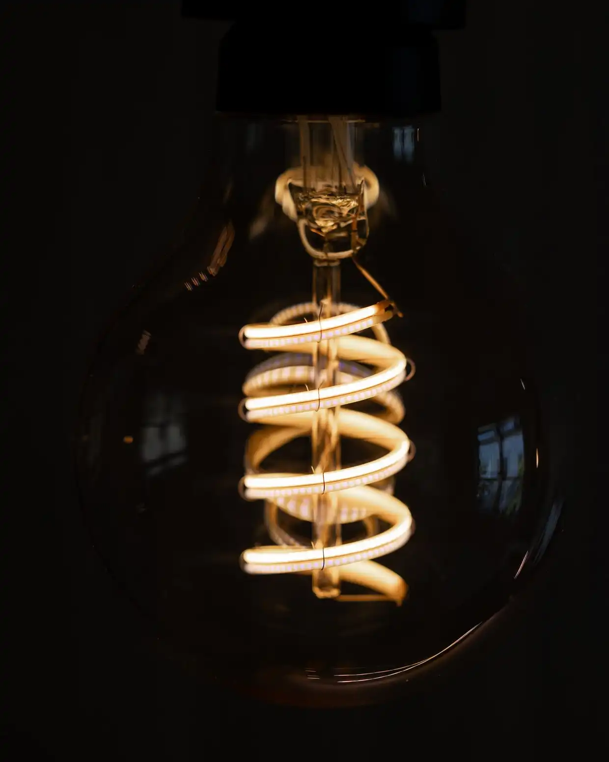 A clear globe bulb with a glowing spiral filament against a dark background