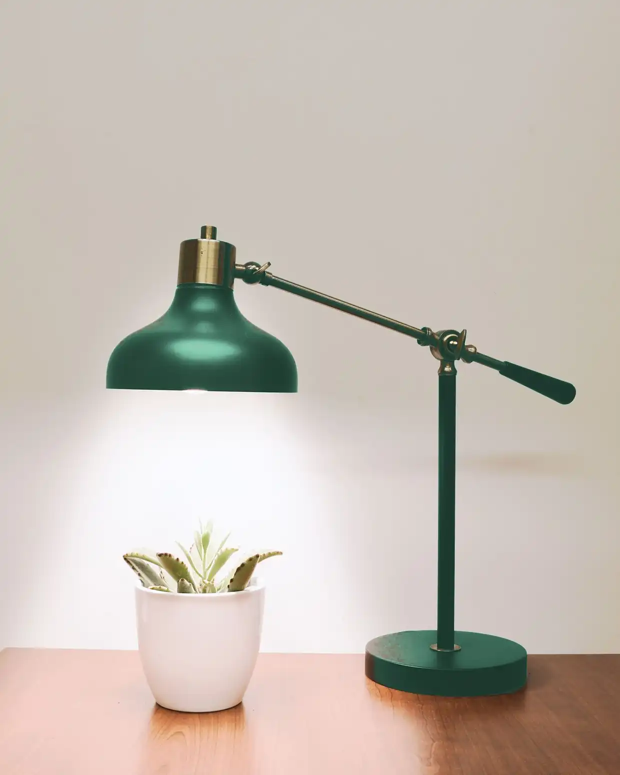 The same desk lamp in a deep fern green finish, with its brass knuckle and counterweighted arm over a wooden desk