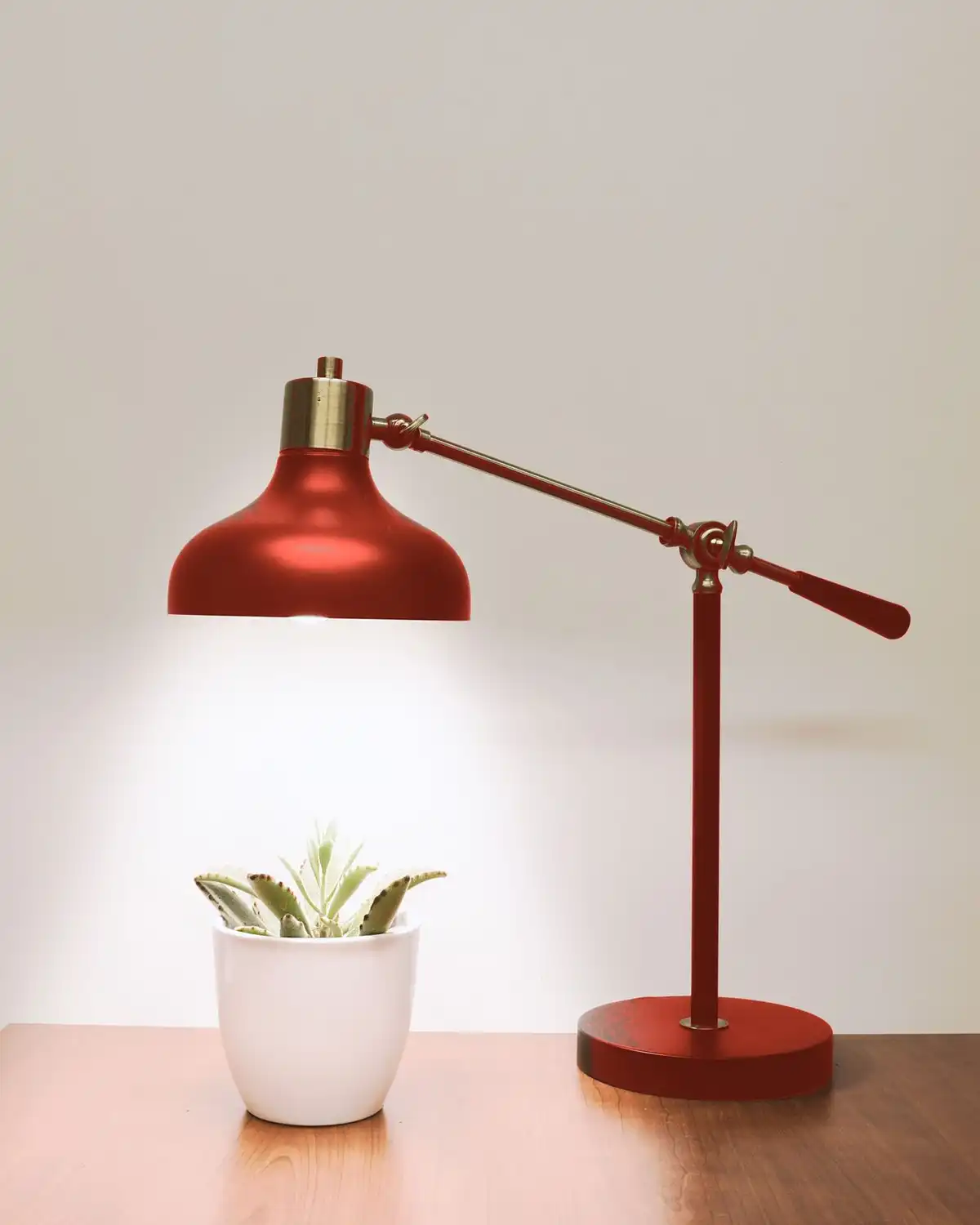 The same desk lamp in an oxide red finish, with its brass knuckle and counterweighted arm over a wooden desk