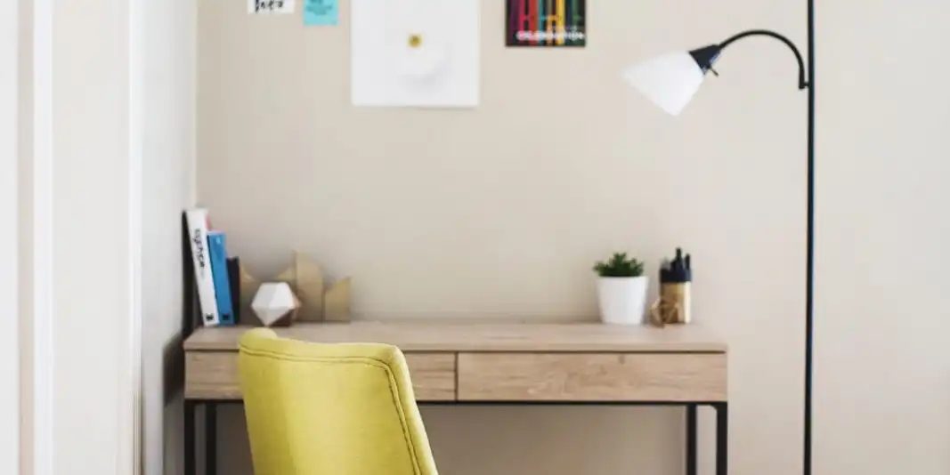 A small writing desk with a yellow chair and a floor lamp in a corner of a room