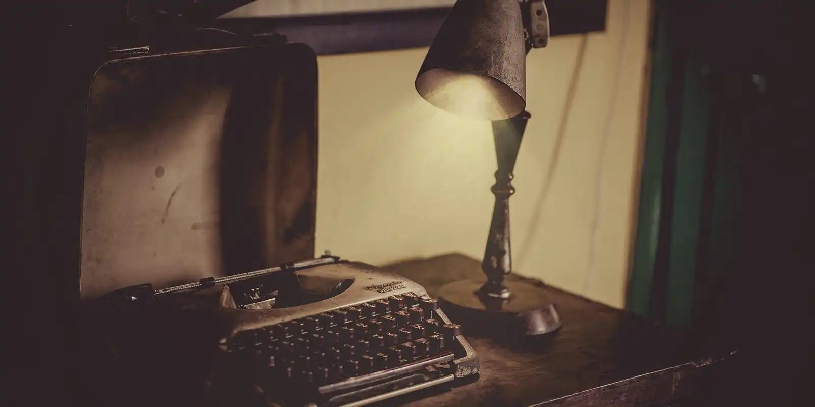 A small desk lamp lighting an old typewriter on a dark wooden desk